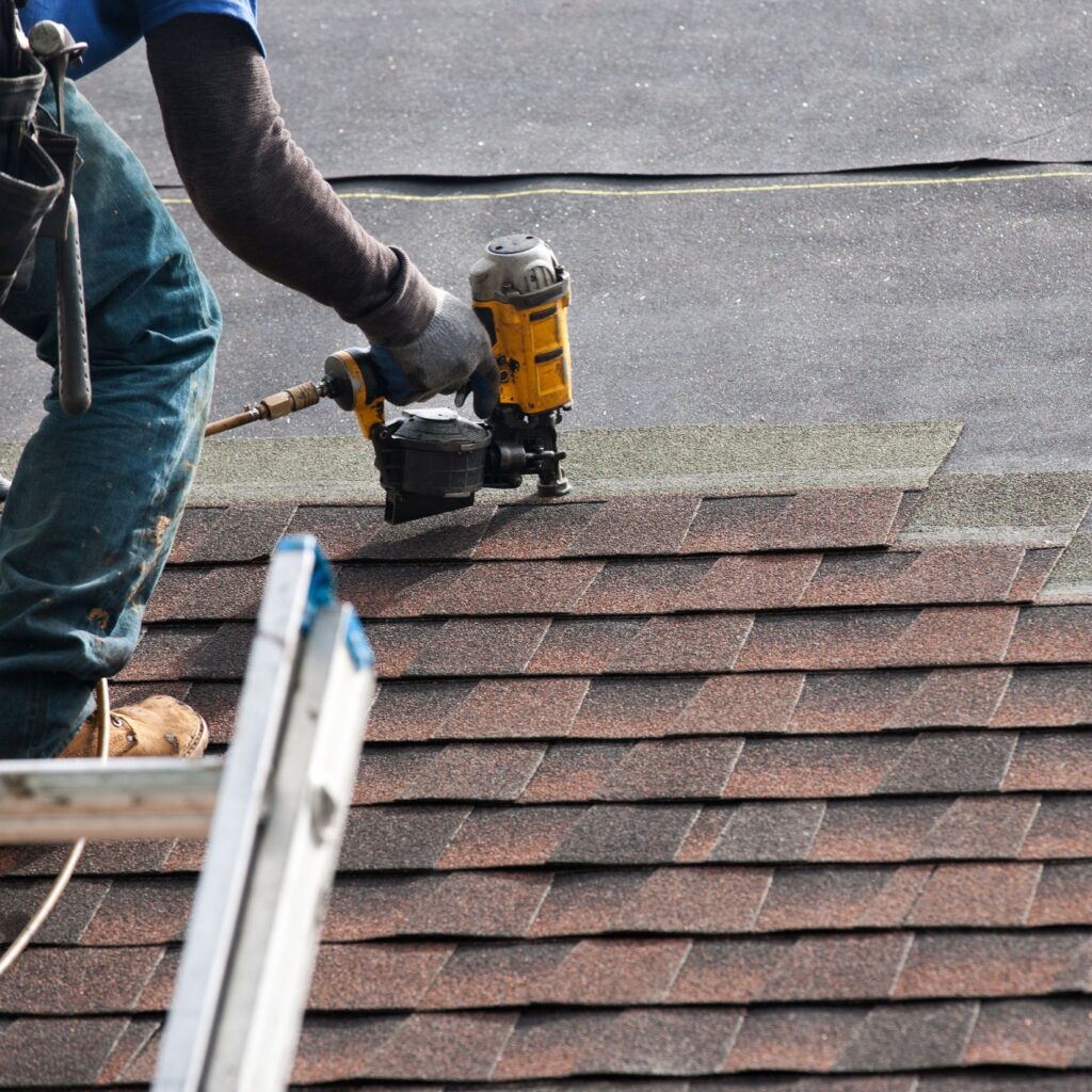 Roofer installing asphalt shingles with nail gun during roof replacement in Philadelphia or South Jersey – NEF Roofing